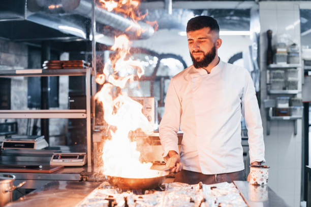 istock Frying pan is on fire. Chef in white uniform cooking food at kitchen. Busy day at work 1330042654