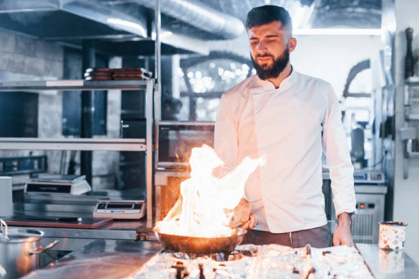 istock Frying pan is on fire. Chef in white uniform cooking food at kitchen. Busy day at work 1330042677