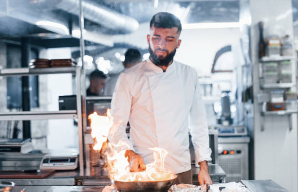 istock Frying pan is on fire. Chef in white uniform cooking food at kitchen. Busy day at work 1330042679