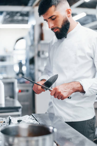 istock Chef in white uniform standing at kitchen. Holding knives in hands 1330043973