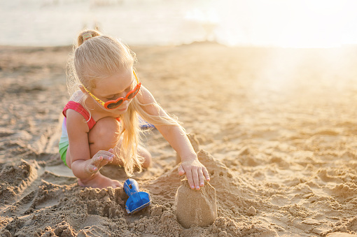 little blonde girl builds a sand castle on the seashore in the evening at sunset in the golden hour in summer. High quality photo