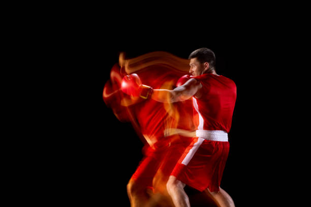 Side view. One young sportsman, professional boxer in gloves training, practicing punches on black studio background in mixed lights. Copyspace for ad.