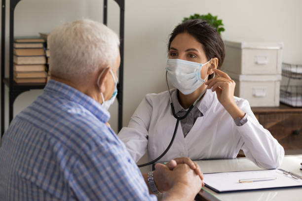 la doctora con mascarilla escucha el corazón de la vieja paciente - chest stethoscope medical exam men fotografías e imágenes de stock