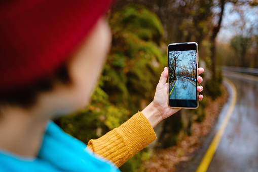 A female hand holding an mobile Phone trying to capture the awesome colors of autumn in the forest. Fall Getaway