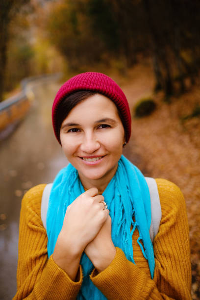 beautiful female hipster in a red hat, yellow sweater and blue scarf walks in the autumn nature. Cool weather. Wanderlust photo series.
