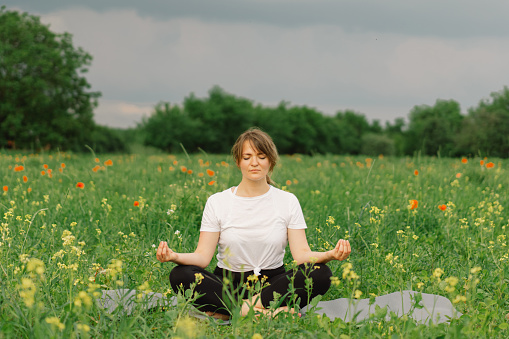 Outdoor image of young Asian/ Indian woman sitting in butterfly position with bare feet and doing yoga at park.
