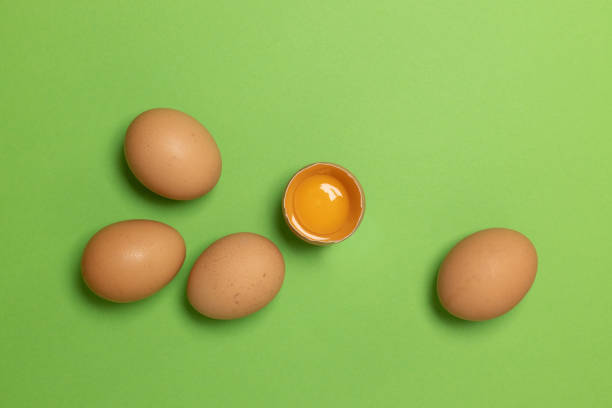 œufs de poule brun de pâques et un œuf cassé avec du jaune sur fond vert - visual art growing photos et images de collection