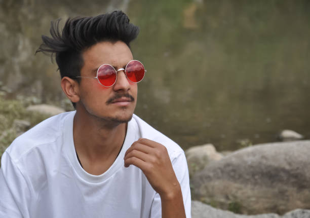 A North Indian handsome young guy sitting beside of river with looking sideways, A guy with wearing white t-shirt and red sunglasses