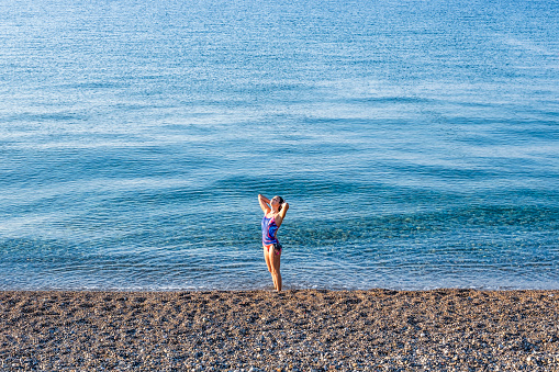 Swim training concept: A teenage girl is preparing for her morning session at the sea. Female sportive swimmer posing standing for the camera. Professional swimming training for the Olympics starting at young age. Swim fashion for ladies.