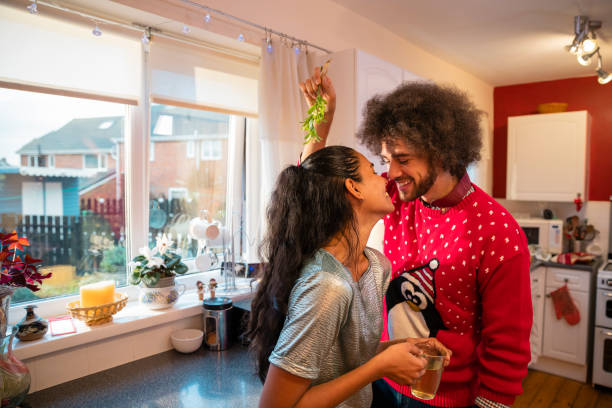 Christmas Romance A shot of a man approaching his wife with a string of mistletoe on Christmas day. They kiss while laughing. They are in the North East of England. kissing on the mouth stock pictures, royalty-free photos & images