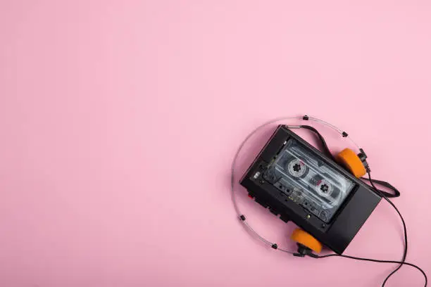 Music listening concept. Vintage cassette tape, audio player and headphones close-up on on pink background top view.