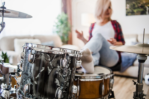 One woman, a shot of a young woman playing drums in her apartment. She is dressed in a plaid shirt, sits at the drums and uses her free time for music.