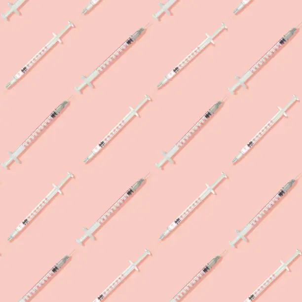 Photo of Contemporary art collage. Small long injection syringes with needles arranged in even rows over pastel pink background.