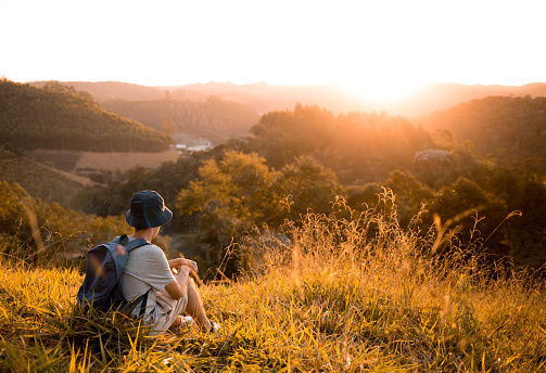 Young man sitting on the grass and watching the sunset in the mountains.