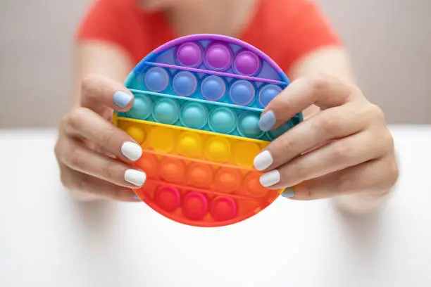 Photo of Rainbow sensory fidget isolated in the hand on white background. New trendy silicone toy.