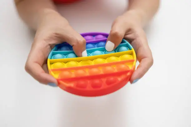Photo of Rainbow sensory fidget isolated in the hand on white background. New trendy silicone toy. Antistress pop it toy.