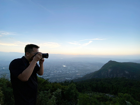 Male tourist using camera to take pictures on top of the mountain