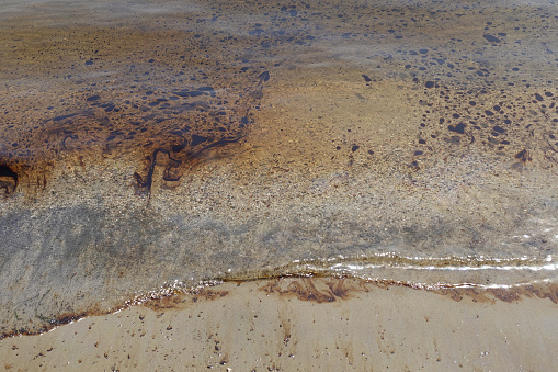 Black tar oil floating on sea water of polluted sandy beach.