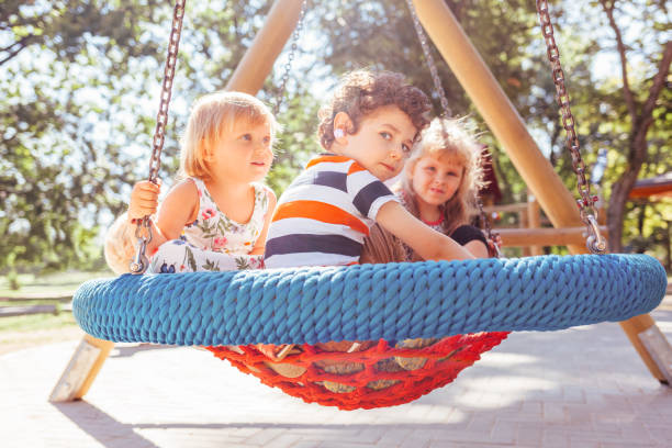 Kids in big swing at the playground. Children playing outdoors.