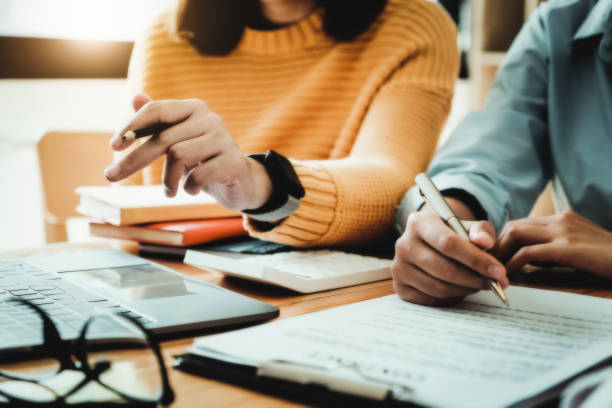 el énfasis está en el consultor de camisa amarilla que sostiene un lápiz y el propietario del negocio que sostiene un bolígrafo que lee los términos de un contrato de empresa conjunta con una empresa asociada. - writing fotografías e imágenes de stock