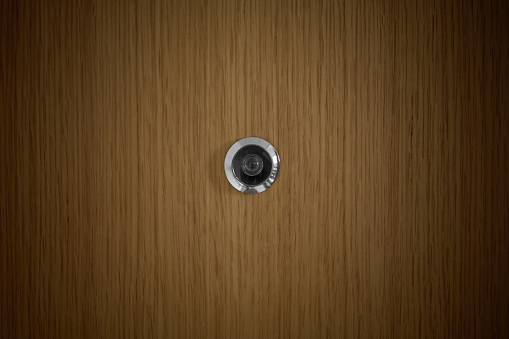 detail of a metal peephole in the center of an oak door