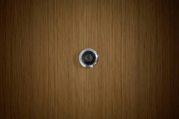 Photo of metal peephole in the center of an oak door