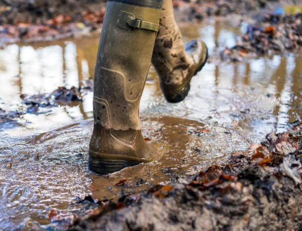 Welly boots - enjoying wet weather Close-up on a pair of feet protected by welly boots as their owner steps enthusiastically through a muddy puddle. mud photos stock pictures, royalty-free photos & images