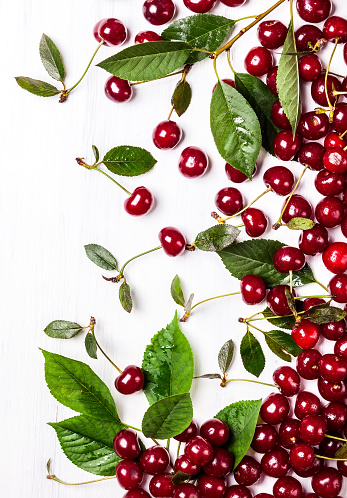 Fresh ripe cherry with green leaves on the white wooden background. Top view, copy space