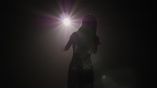 Silhouette of a luxurious singer in an evening gown on a stage in the dark.