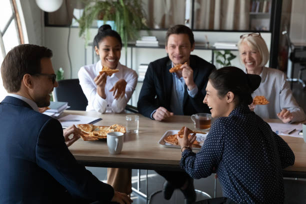 happy diverse coworkers enjoying pizza party at office meeting table - pizza eating african descent lunch imagens e fotografias de stock