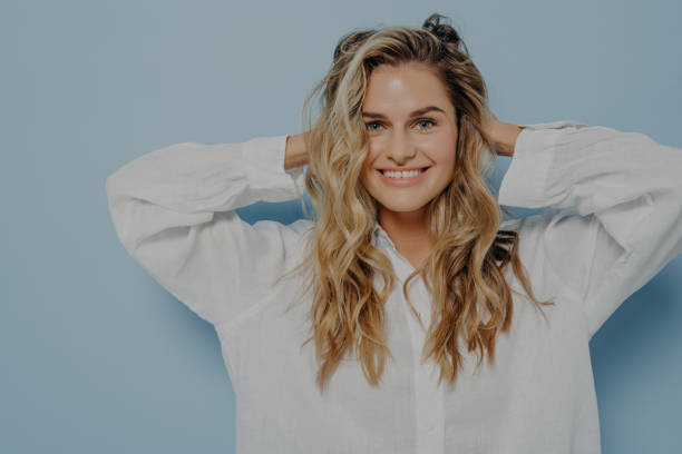Joyful blonde woman holding her head in excitement Joyful blonde woman with long wavy hair holding head with both hands in excitement, can not contain happiness and joy, standing isolated next to light blue background. Happy emotions concept wavy hair stock pictures, royalty-free photos & images