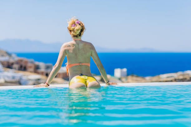 Woman enjoying view from endless swimming pool, Elia, Mykonos island, Cyclades, Greece. Model and Property released.