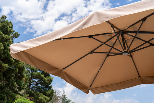 Sunshade awnings tent with sky and trees. Beige parasol in summer sunshine