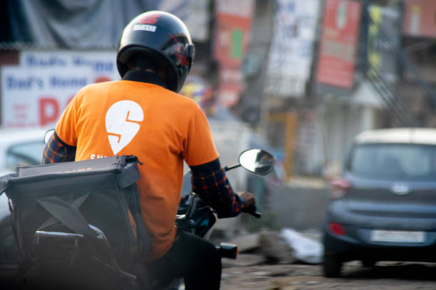 bike rider with helmet and a swiggy tshirt showing the rapid growth of food delivery e-commerce startups unicorns decacorns and the workers who are provided jobs by them stock photo