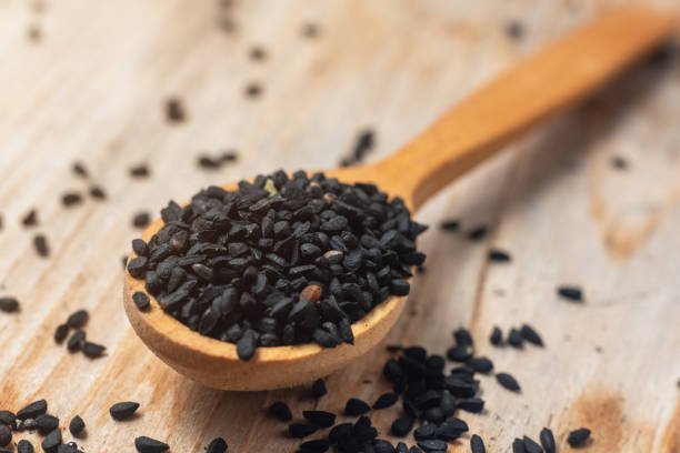 Black cumin seeds on wooden spoon on wooden background Black cumin seeds on wooden spoon on wooden background. caraway stock pictures, royalty-free photos & images