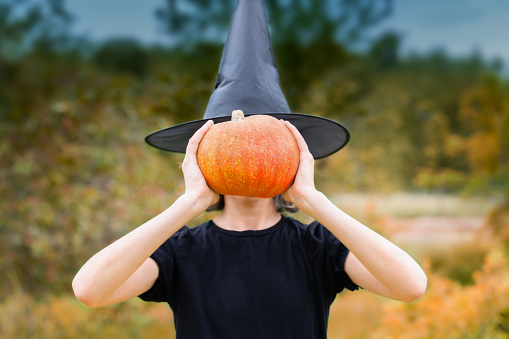 Halloween witch in black hat holding a pumpkin instead of her head