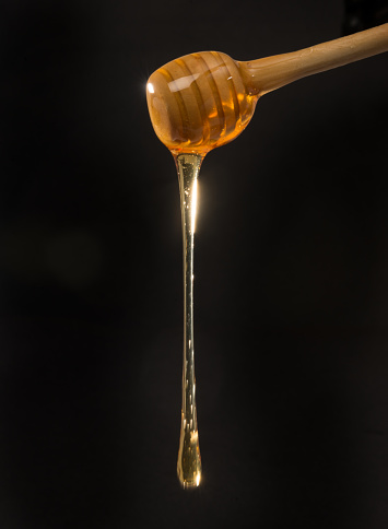close-up detail of cooling spoon, dripping honey. studio photo, black background.