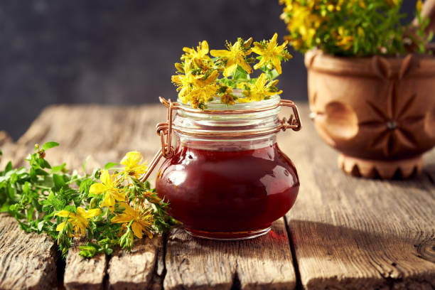 un frasco de aceite de hierbas rojas hecho de flores de hierba de san juan - mortar and pestle wood healthcare and medicine jar fotografías e imágenes de stock