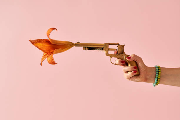 花が出てくる金色の偽の銃から撃つ女性の手 - gun women handgun armed forces ストックフォトと画像