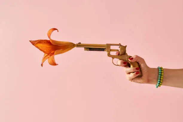 Photo of Woman's hand shooting from a gold painted fake gun with a flower coming out