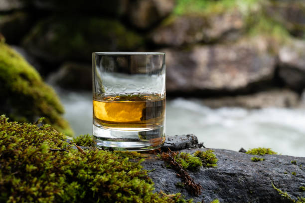 glass of strong scotch single malt whisky with fast flowing mountain river on background - spey scotland stockfoto's en -beelden