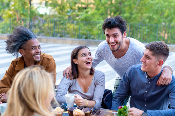 gruppo multietnico di studenti universitari che fa colazione in mensa, giovani amici sorridenti e ridendo mentre bevono caffè e mangiano muffin - coffee couple italy drinking foto e immagini stock