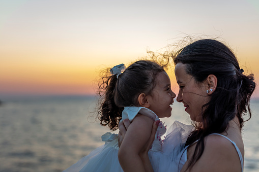 Mother and daughter have fun and laugh from pier at sunset