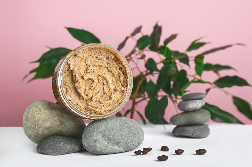 Coffee body scrub and coffee beans on pink background. Skincare, health care concept.