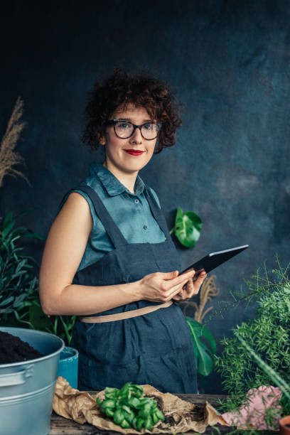 istock Cheerful Woman Florist Using Digital Tablet while Working at her Flower Shop 1330109205
