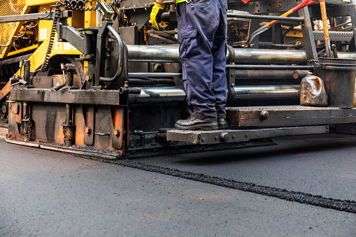 resurfacing residential road with asphalt paving machine and worker raking asphalt