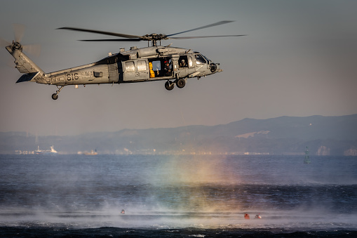 Yokosuka, Kanagawa Prefecture, Japan - January 20, 2021: A US Navy MH-60 helicopter with rescue swimmers trains off the coast with a stretcher in the water.