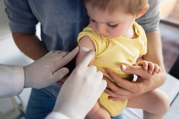 One unrecognizable doctor putting a patch on the little boy's shoulder after successful vaccination stock photo