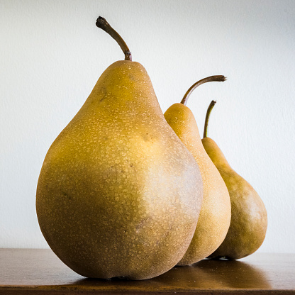 Artistic presentation of three pears in a square format. Simple golden color on light background and sitting on a wooden table.