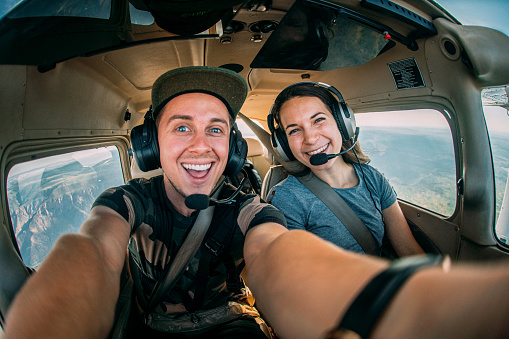 Wide Angle Selfie Fisheye Shot of Two Cheerful Young Adult Male and Female Friends Together in the Cockpit Flying a Small Single Engine Airplane